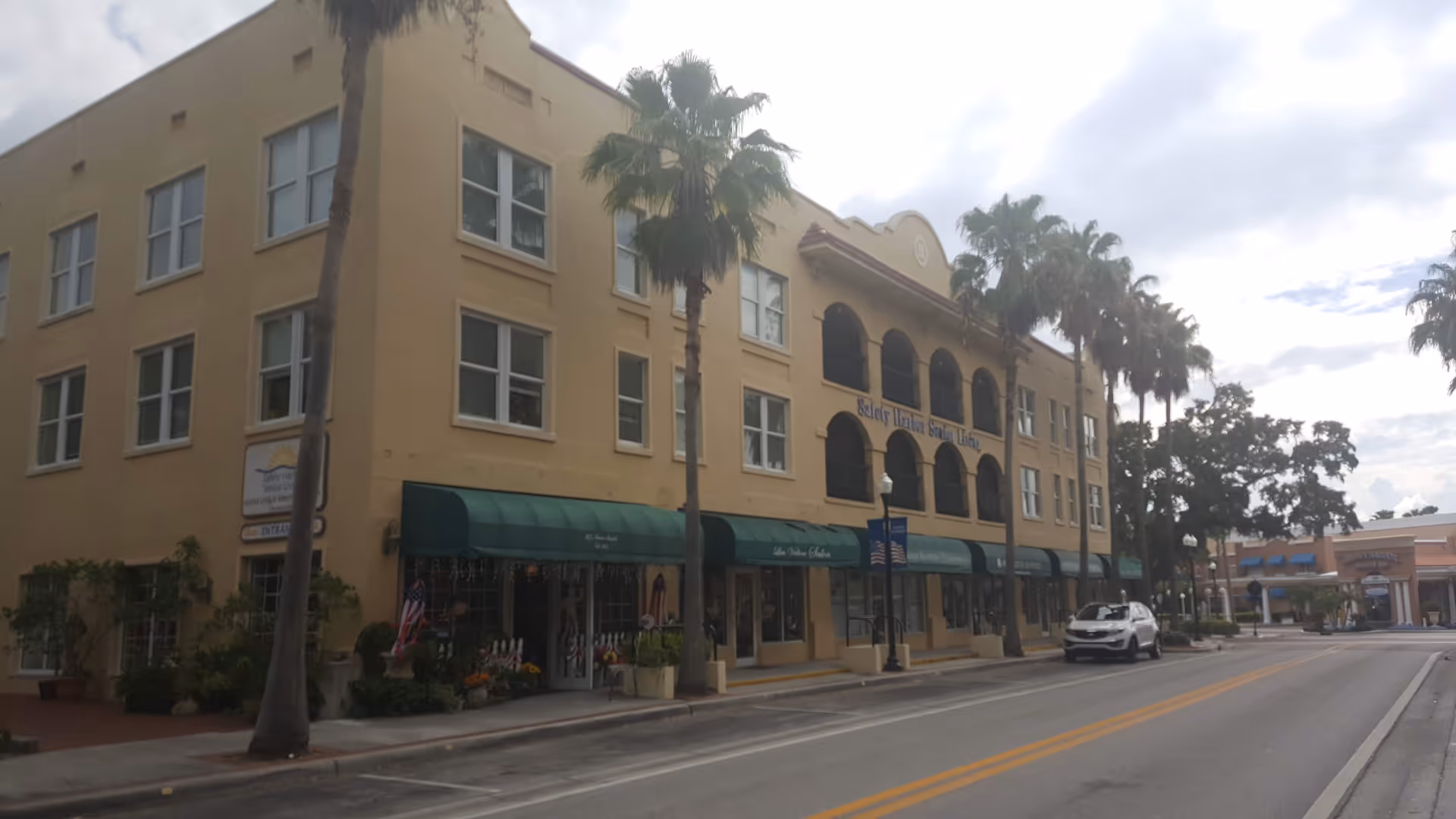 Exterior view of Safety Harbor Senior Living with green awnings and palm trees along a street.