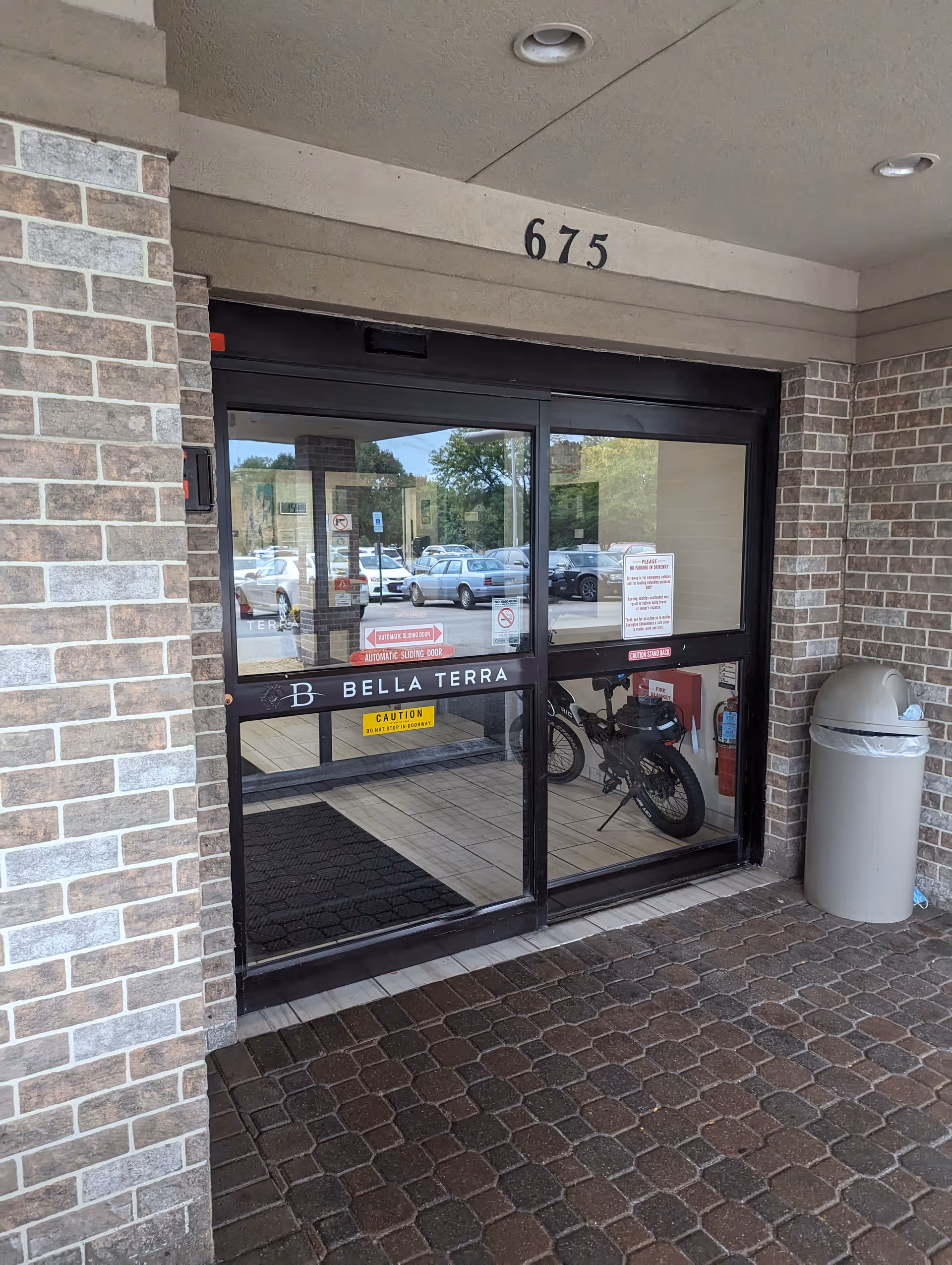 Entrance to Bella Terra Schaumburg with glass doors, brick walls, and a bicycle inside.