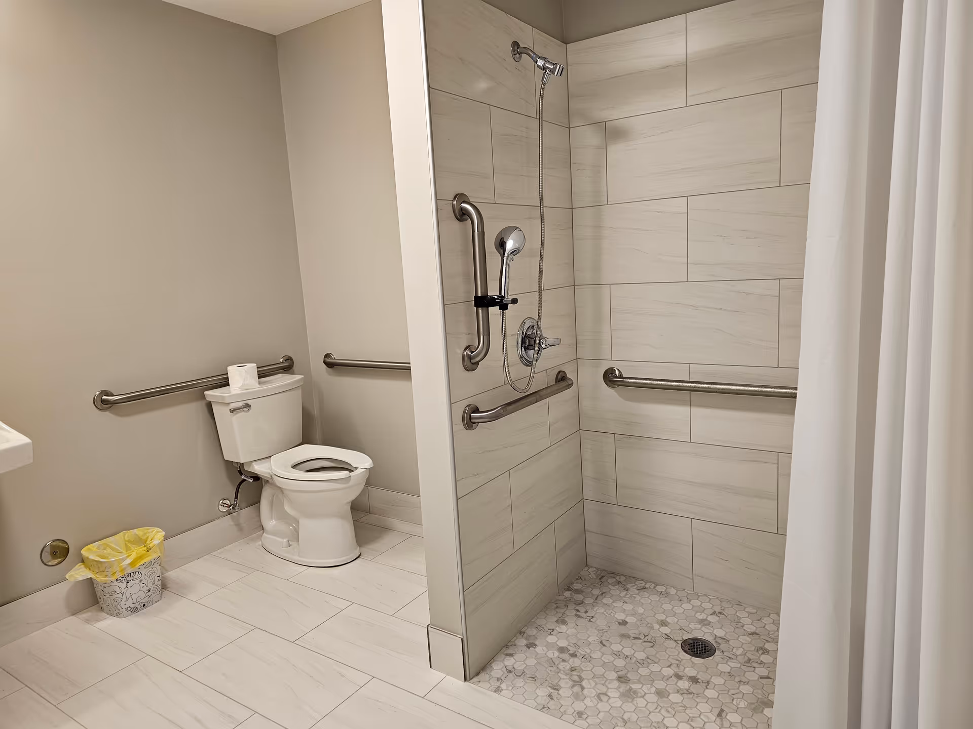Accessible bathroom with walk-in shower, grab bars, toilet, and tiled floor