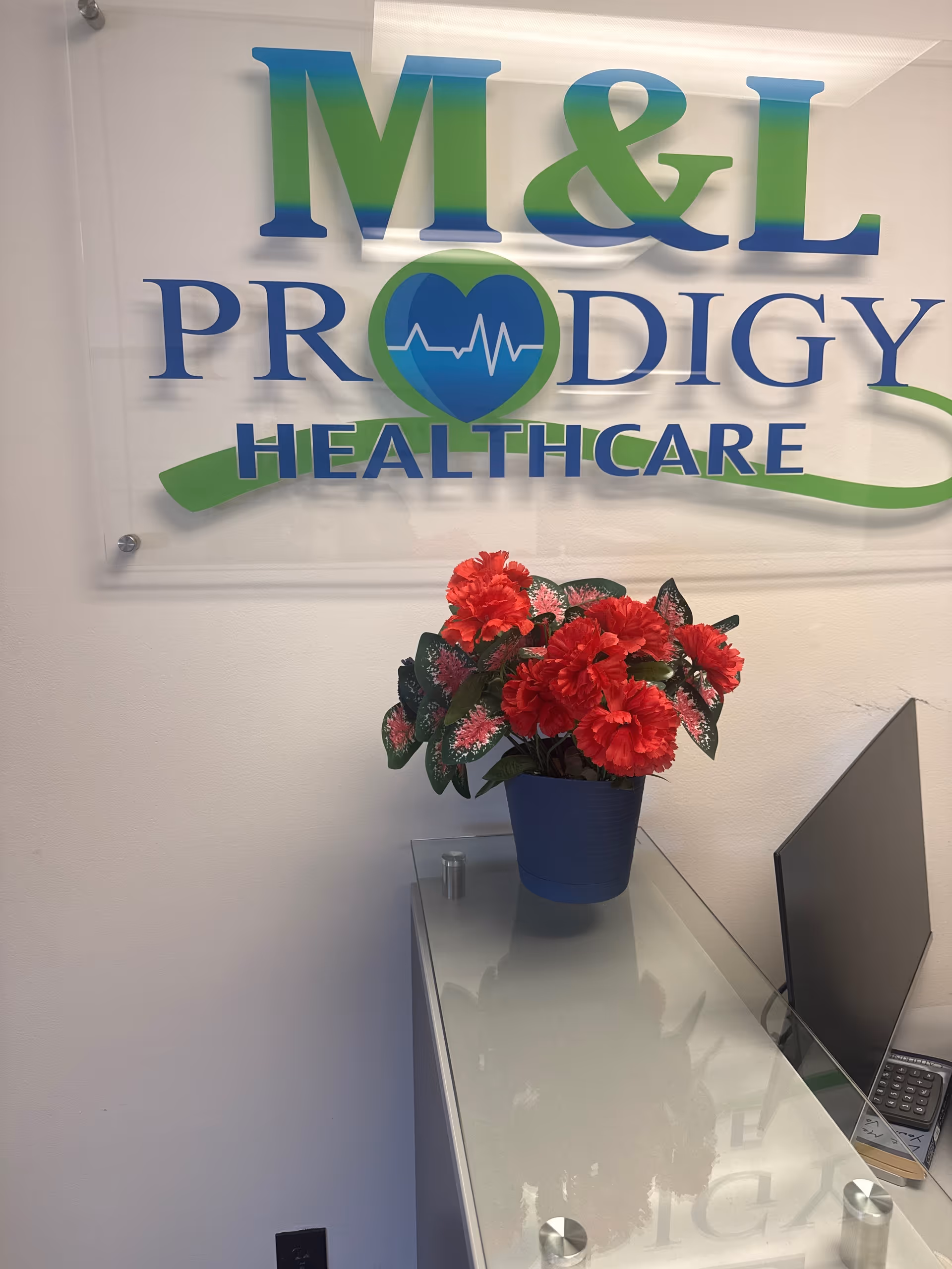 Reception area with M&L Prodigy Healthcare sign, desk, computer, and red flowers.