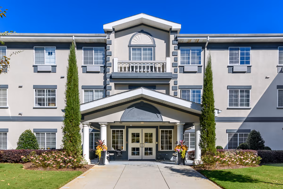 Front exterior of a multi-story senior living home with columns and landscaped entrance.