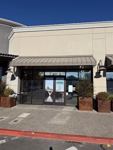 Exterior storefront of Riverside Home Health Care & Hospice with glass doors and planters.