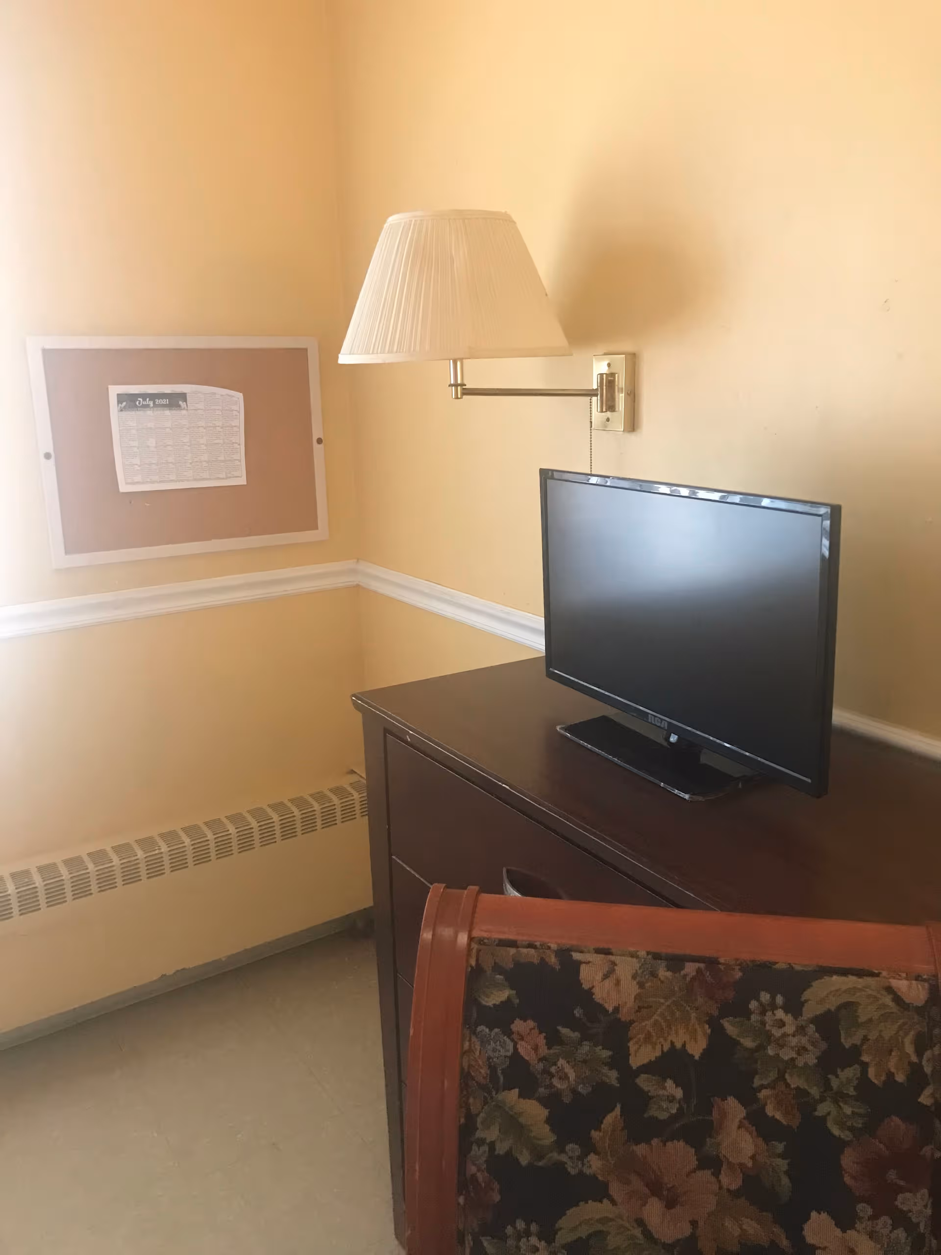 Interior room with desk, TV, lamp, bulletin board, and floral chair.