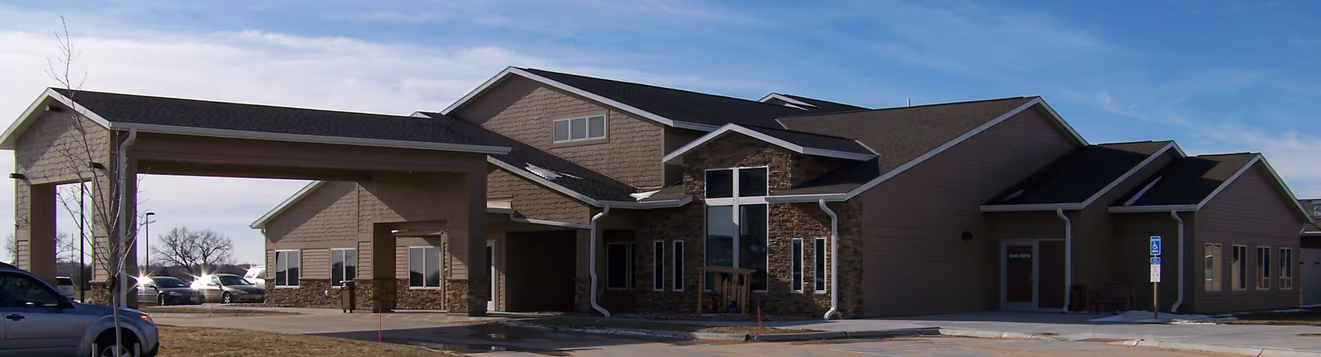 Exterior view of a beige senior living facility with a covered entrance and parking.