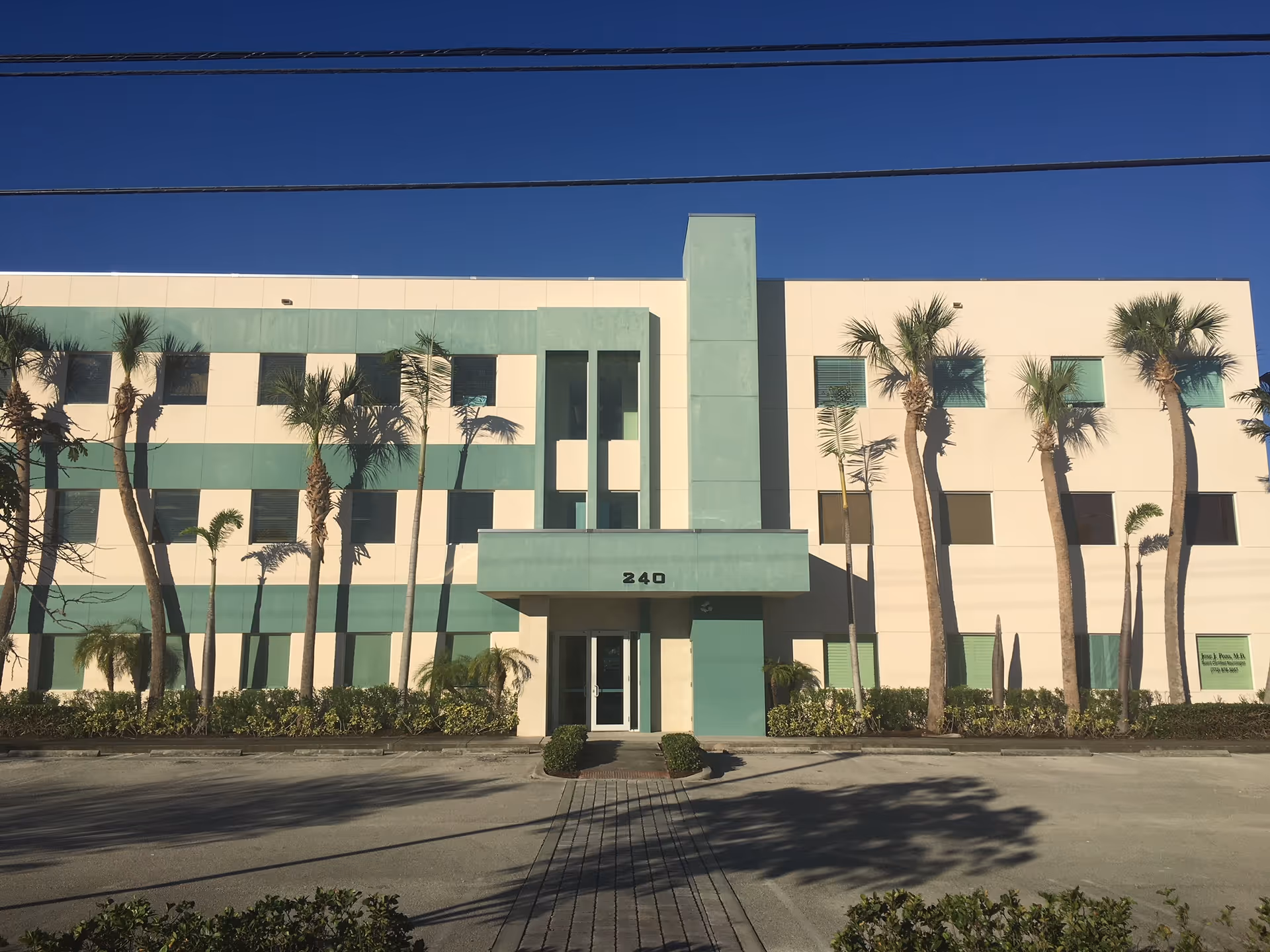 Exterior view of a modern, teal-accented building with palm trees and a driveway.
