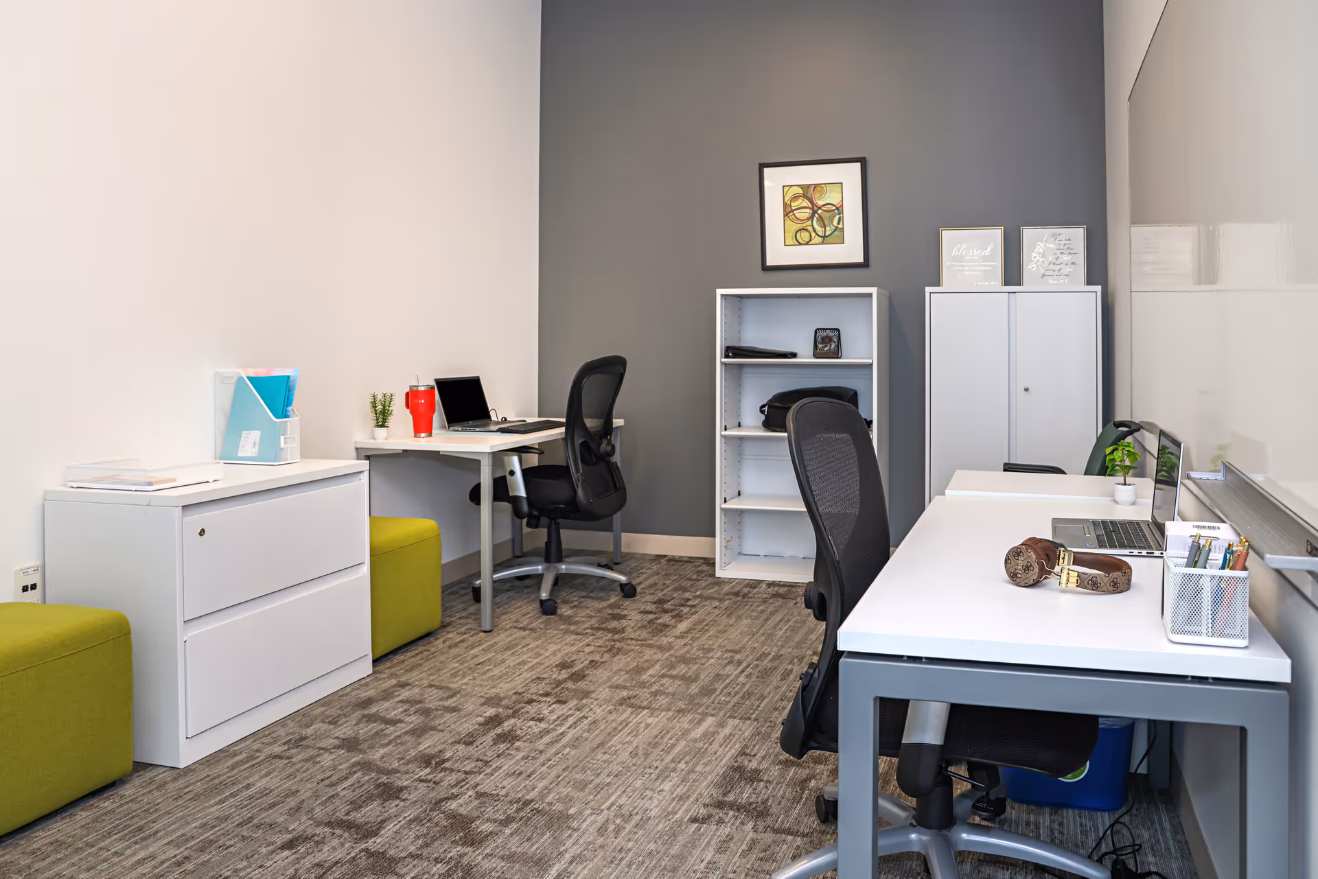 Office area with desks, chairs, filing cabinet, shelves, and decorative art in a modern senior facility.