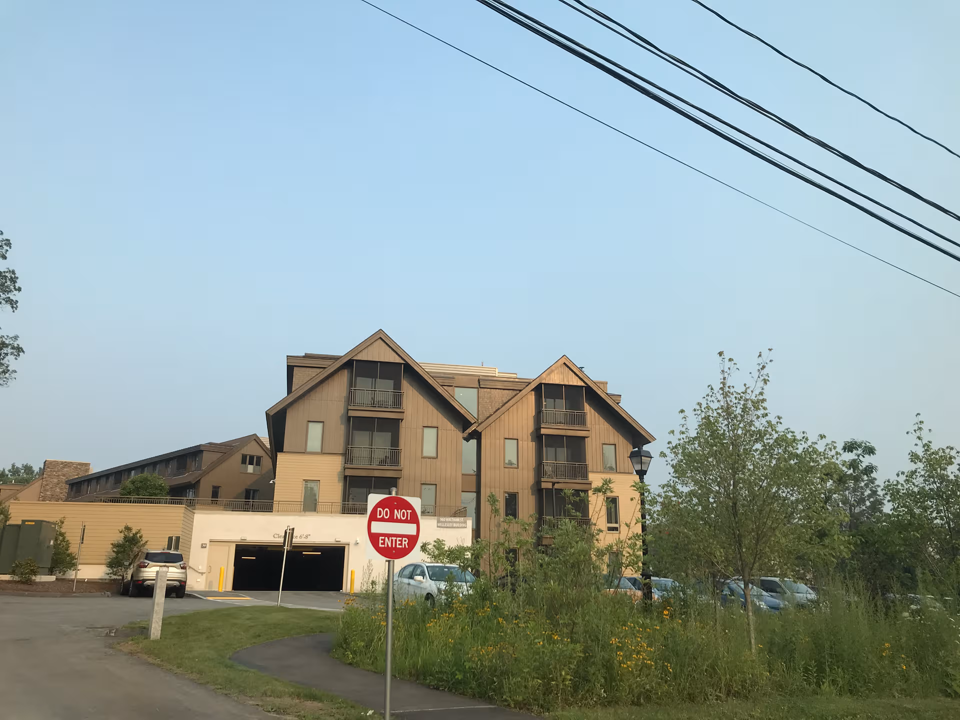 Two-story brown senior living building with balconies, driveway, and surrounding trees.