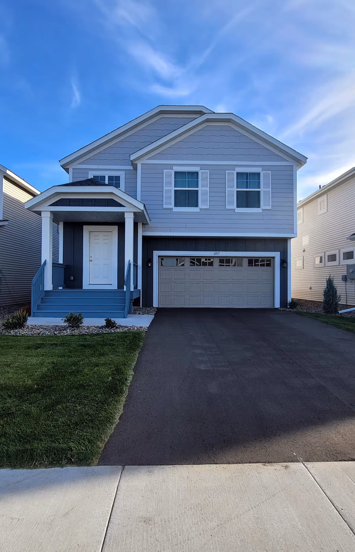 Blue two-story suburban house with a front porch, stairs, and attached two-car garage.