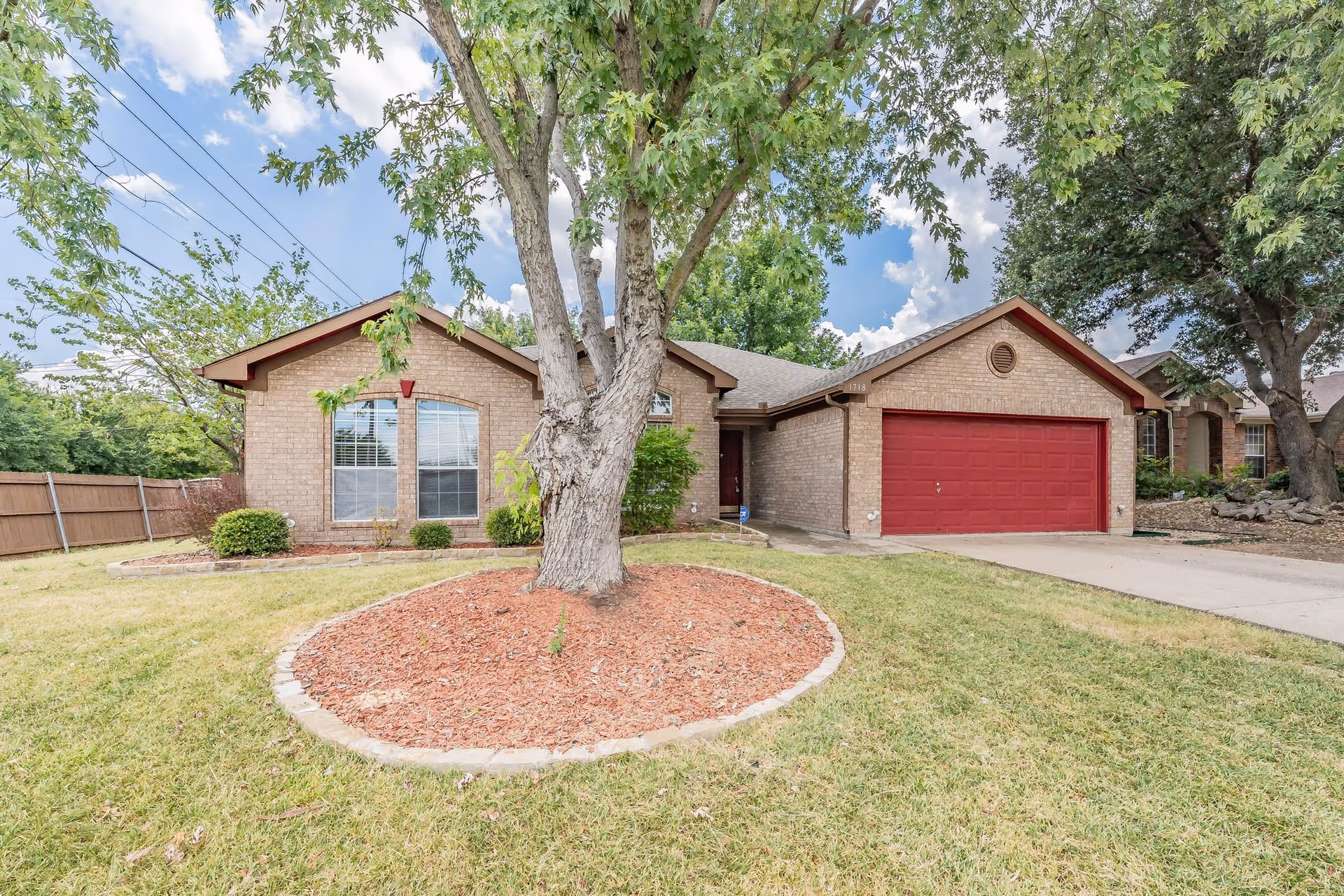 Single-story brick facility with a red garage door, front yard, and large tree.