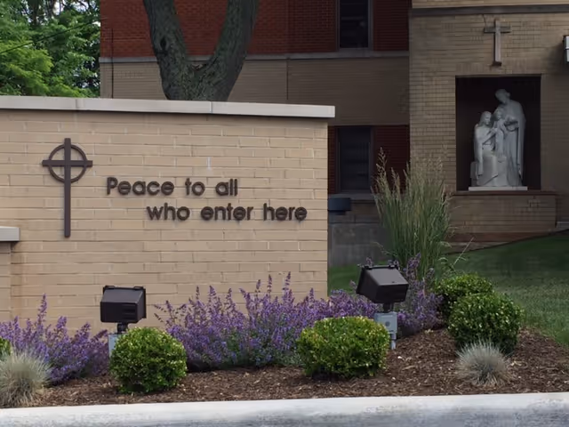 Exterior view of a brick building with a sign reading 'Peace to all who enter here'.