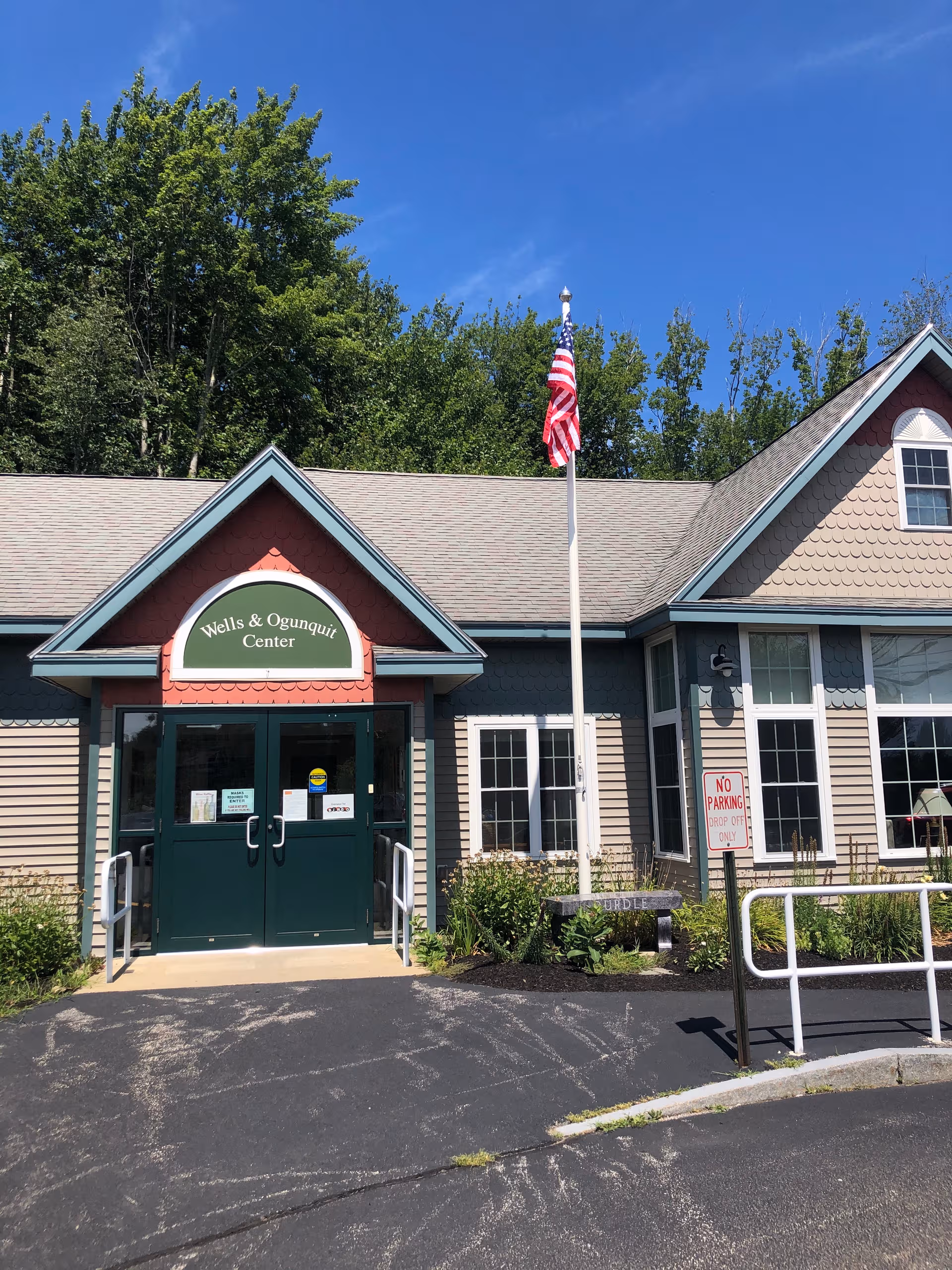 Avita of Wells exterior entrance with green doors, flagpole, and Wells Ogunquit Center sign.