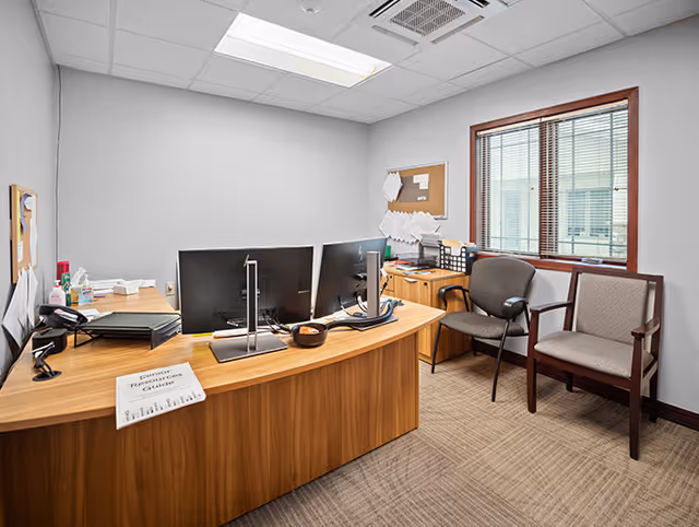 A tidy office with desks, computers, and seating in a medical facility.
