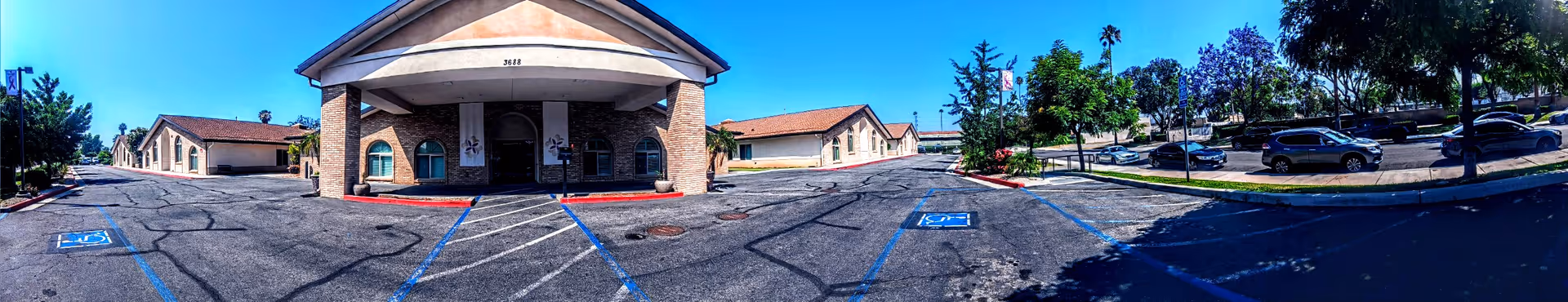Panoramic view of Arlington Gardens Care Center exterior, showing the entrance, parking lot, and trees.
