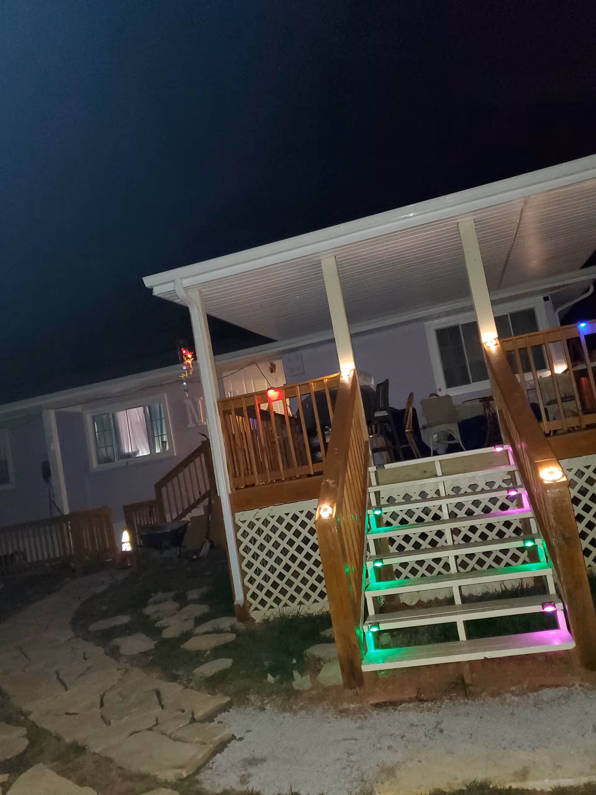 Night exterior of a wooden deck with colorful-lit stairs and outdoor seating.