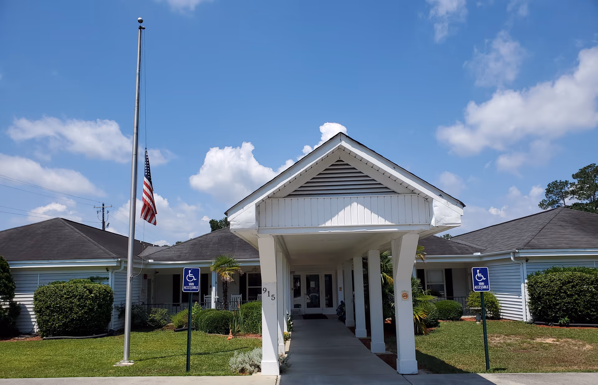 Front entrance of Jenni-Lynn Assisted Living with walkway, flag, and handicap signs.