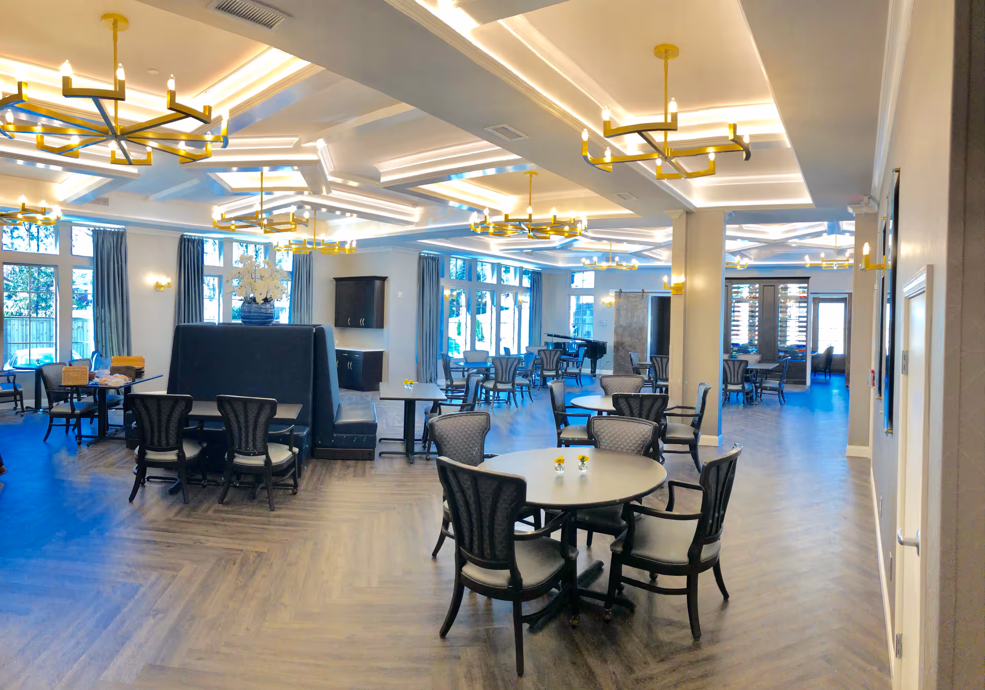 Bright interior dining and lounge area with round tables, chairs, and gold chandeliers.