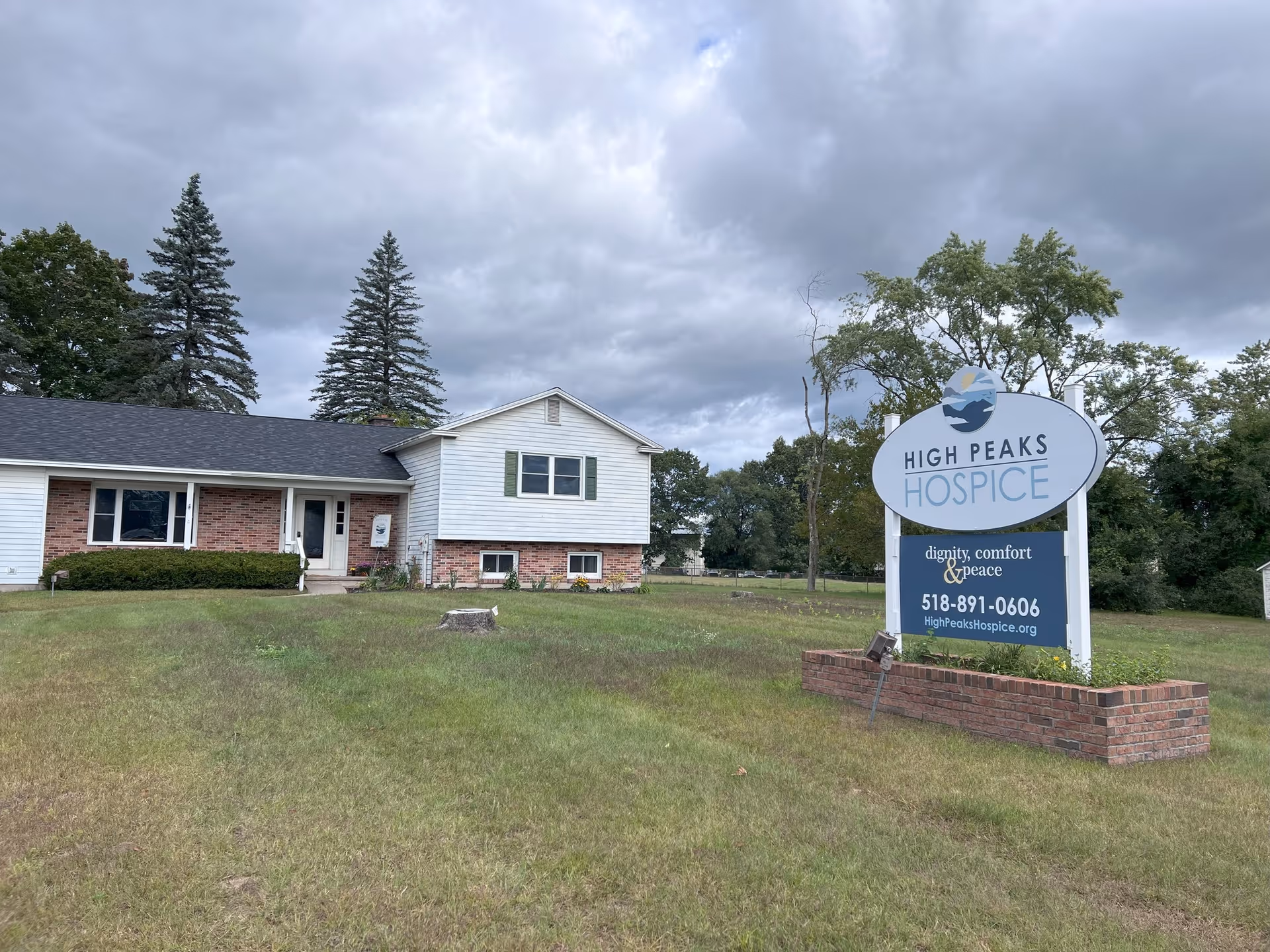 Exterior view of High Peaks Hospice facility with a large front sign on a grassy lawn.