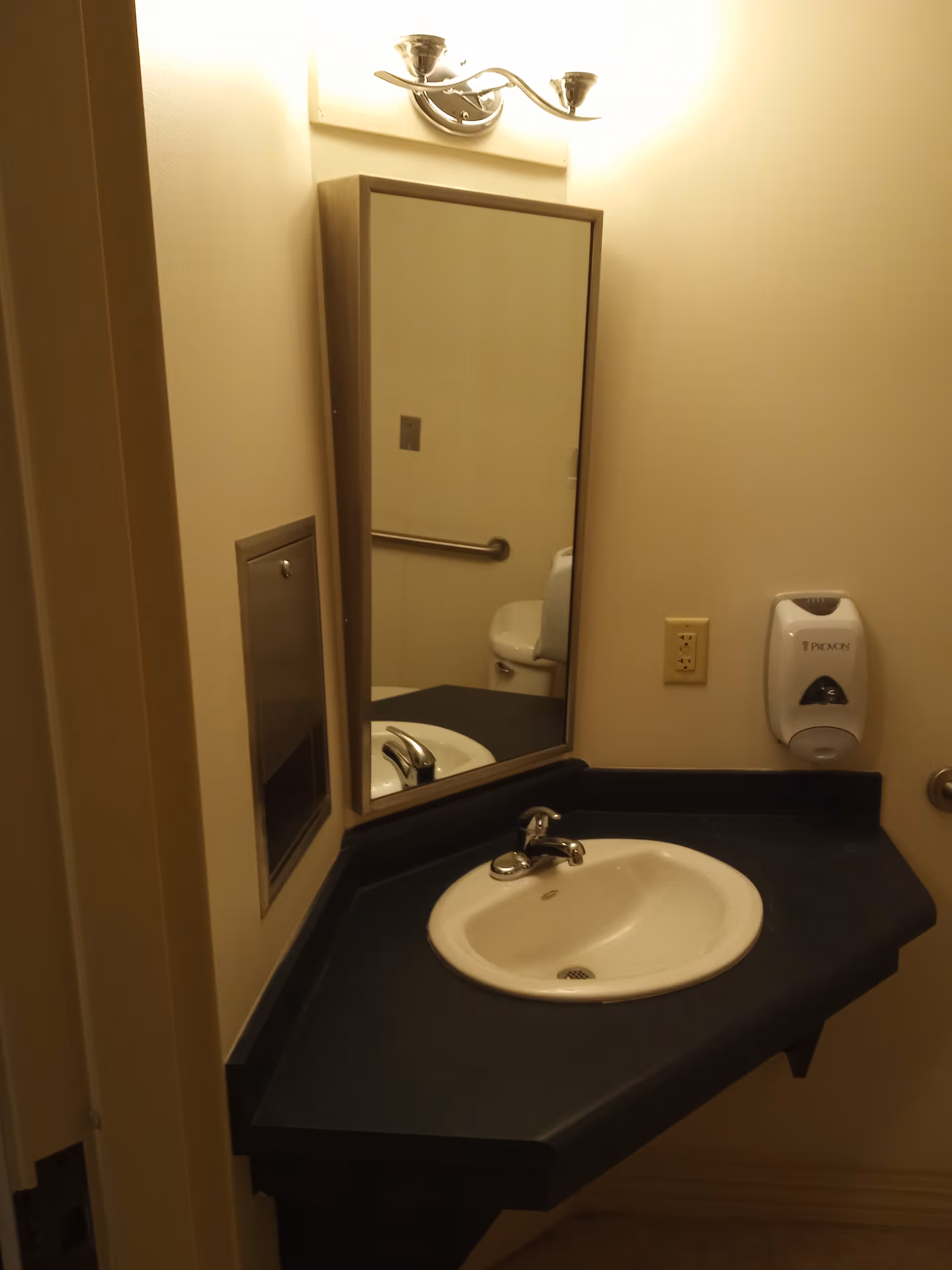 Bathroom sink with mirror, light fixture, and wall-mounted soap dispenser.