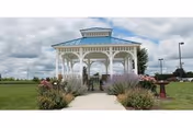 A pastel blue gazebo on a grassy lawn with flowering shrubs and a walkway.
