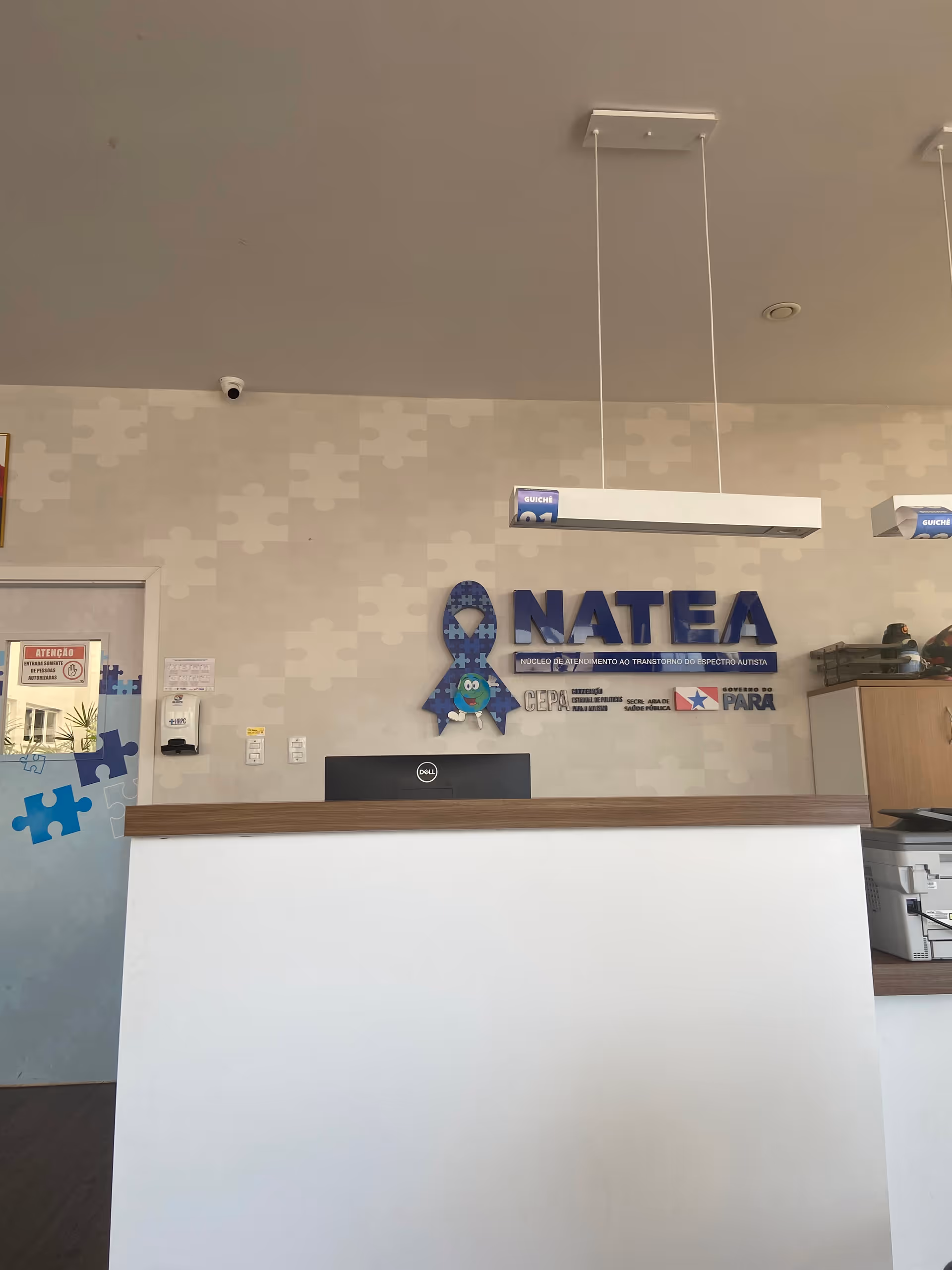 Reception desk in a modern lobby with puzzle-pattern wall and a sign behind.
