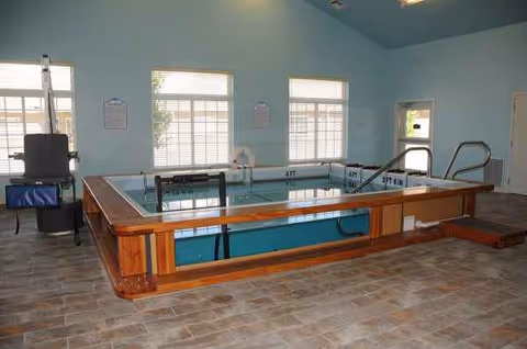 Indoor therapy pool with wooden frame inside a blue-walled senior living facility.