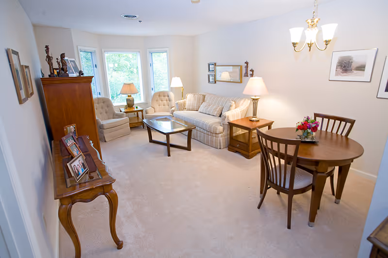 Light-filled living room with a sofa and armchairs around a coffee table, a small round dining table, and decorative wooden furniture.