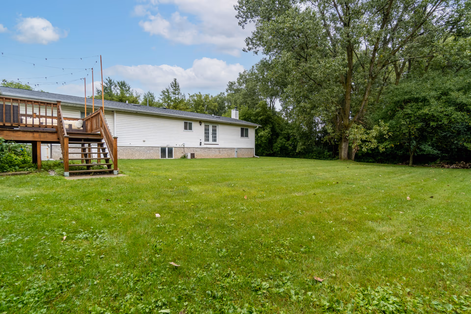 A single-story housing facility with a wooden deck and a large grassy backyard.