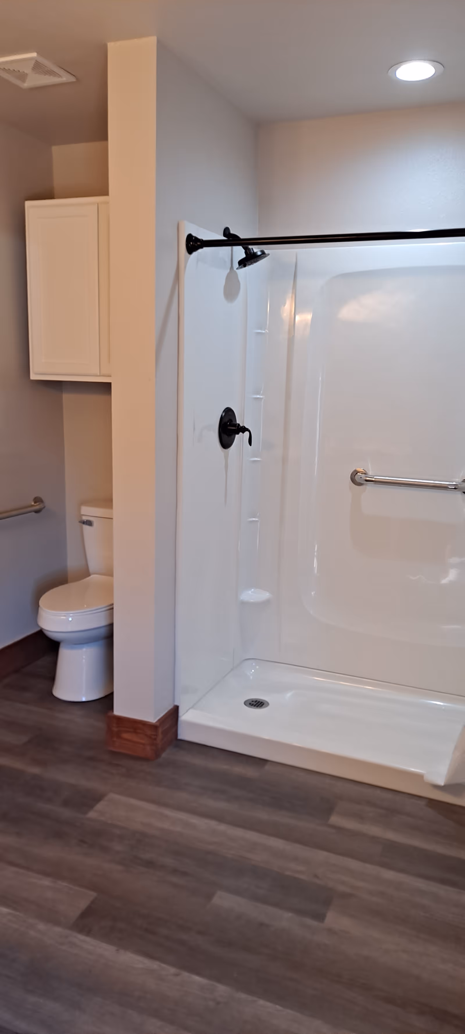 ADA-compliant bathroom with walk-in shower, toilet, cabinet, and grab bars.