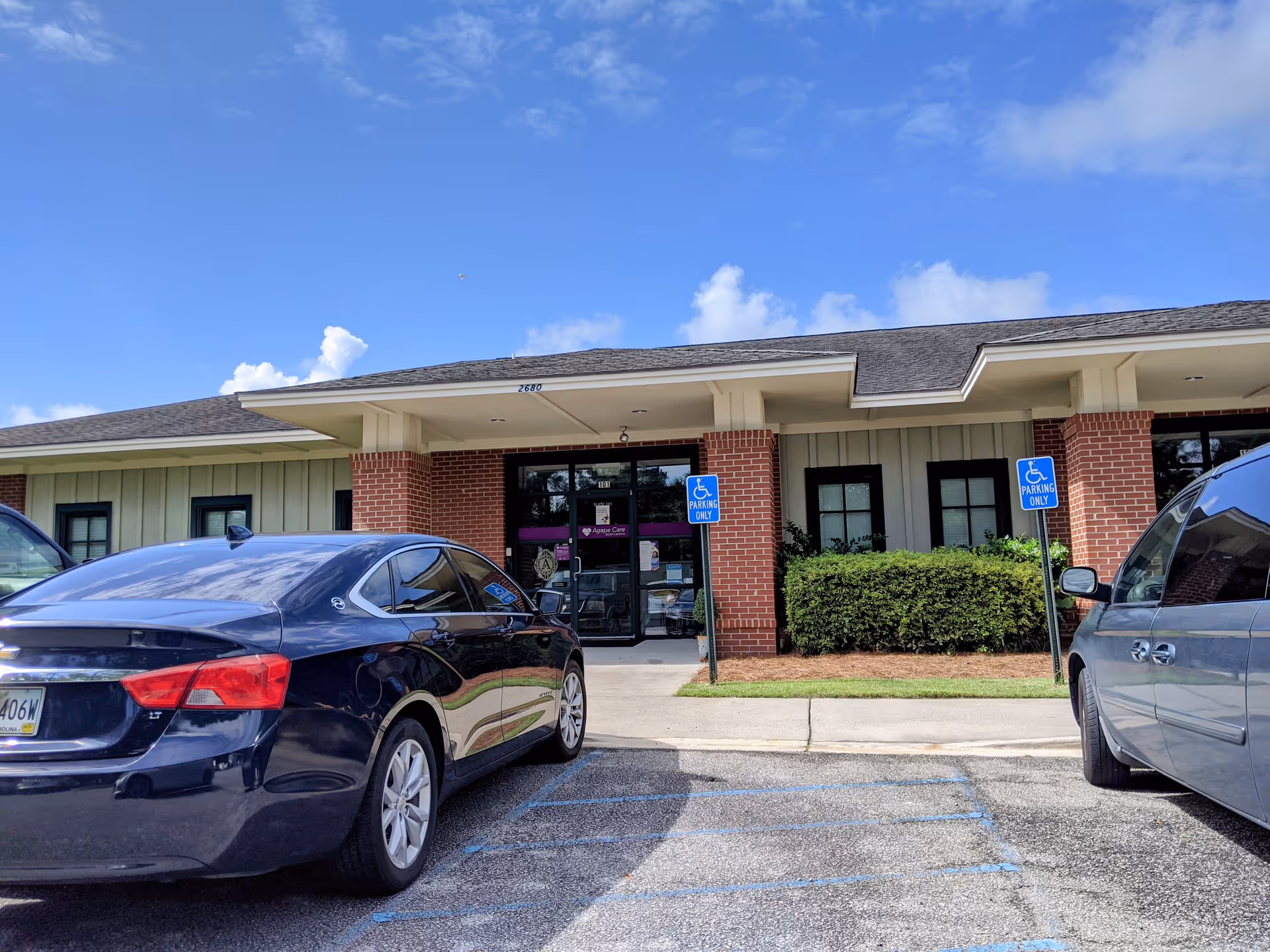 Front exterior of Agape Care South Carolina with entrance, handicap parking signs, and cars.