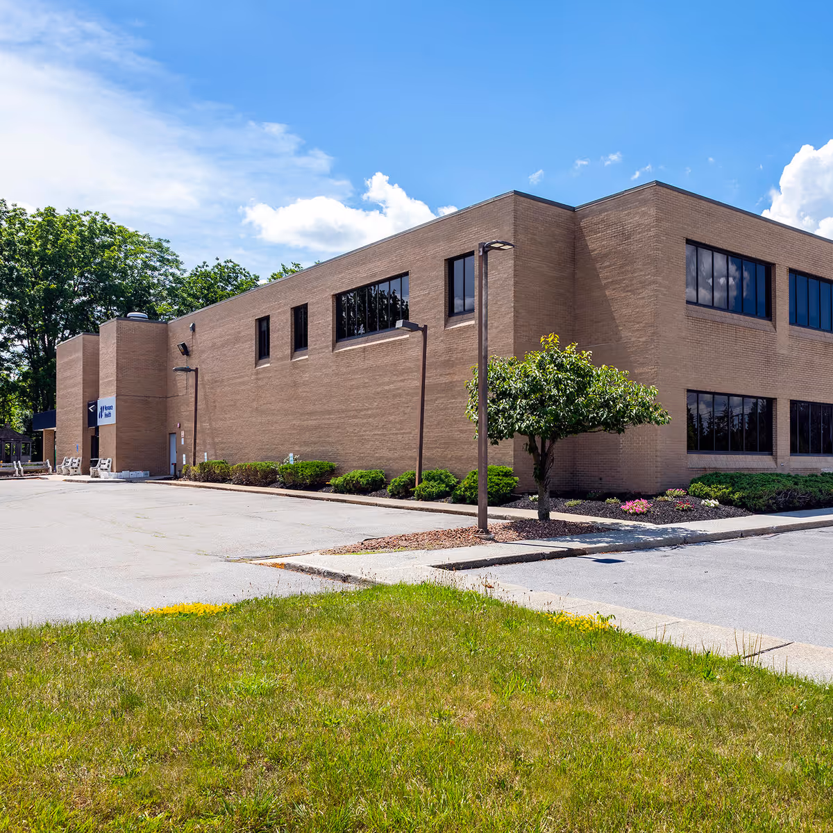 Brick medical practice building exterior with parking lot and landscaping under blue sky.