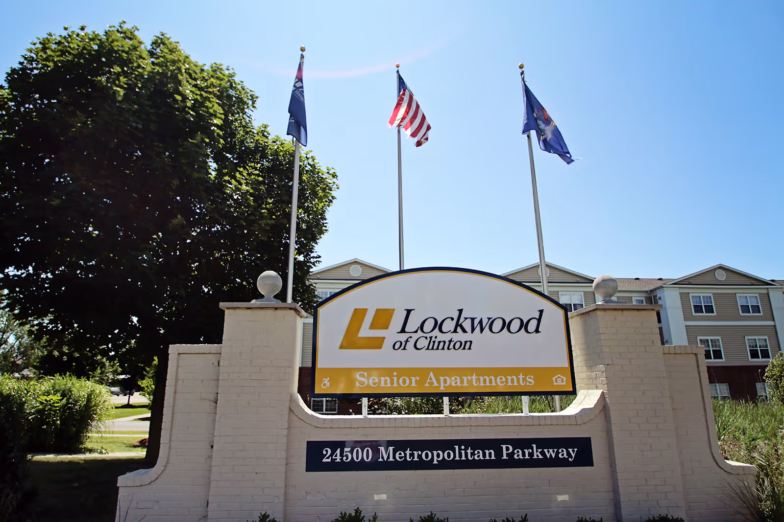 Sign for Lockwood of Clinton Senior Apartments with flags and building behind.