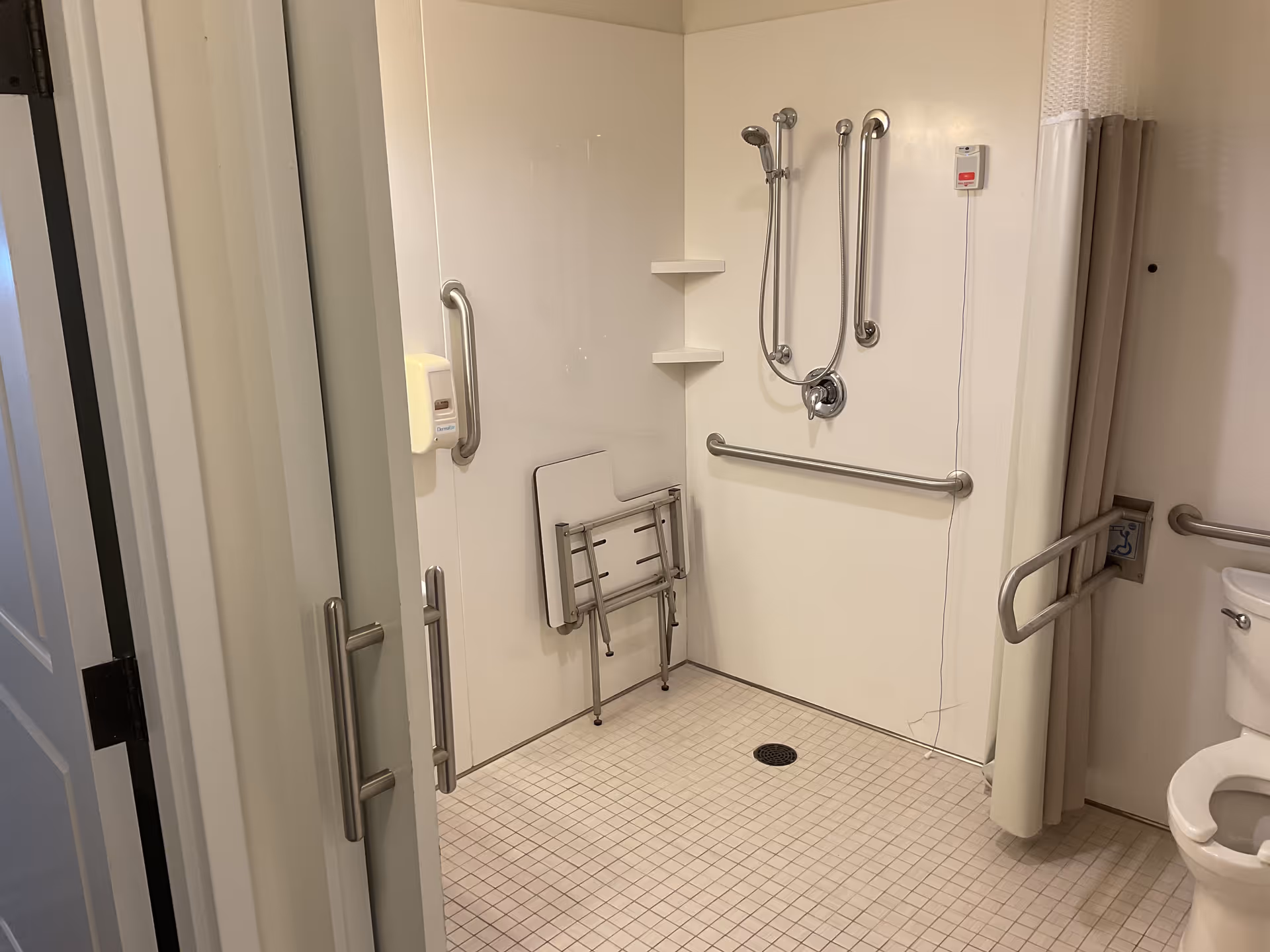 Accessible bathroom with grab bars, shower chair, and tiled floor.