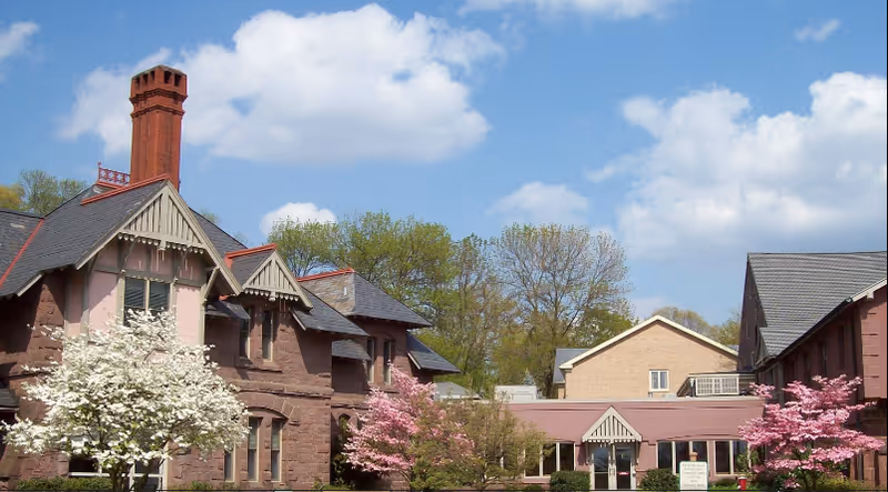Brick senior living facility exterior with blooming trees and a blue sky.