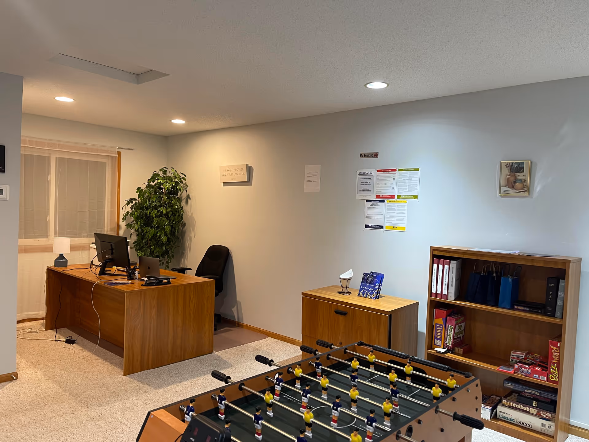 A senior living facility recreation area with foosball table, desk, computer, and shelves.