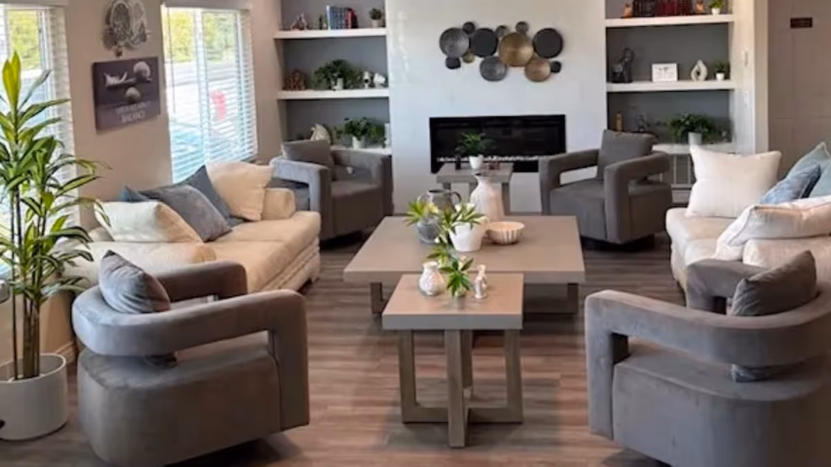 Bright, modern living room in Birch Residence with gray seating, plants, shelves, and a fireplace.