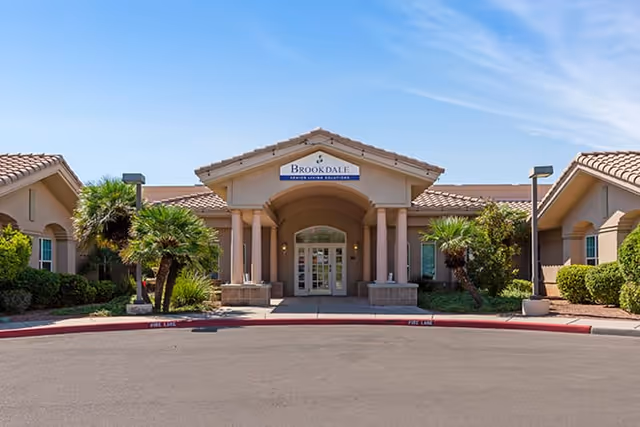 Front exterior view of Brookdale Tanque Verde senior living facility with a covered entrance, palm trees, and clear blue sky.