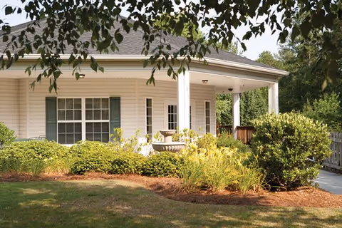 Single-story senior living facility exterior with a covered front porch and landscaped shrubs.