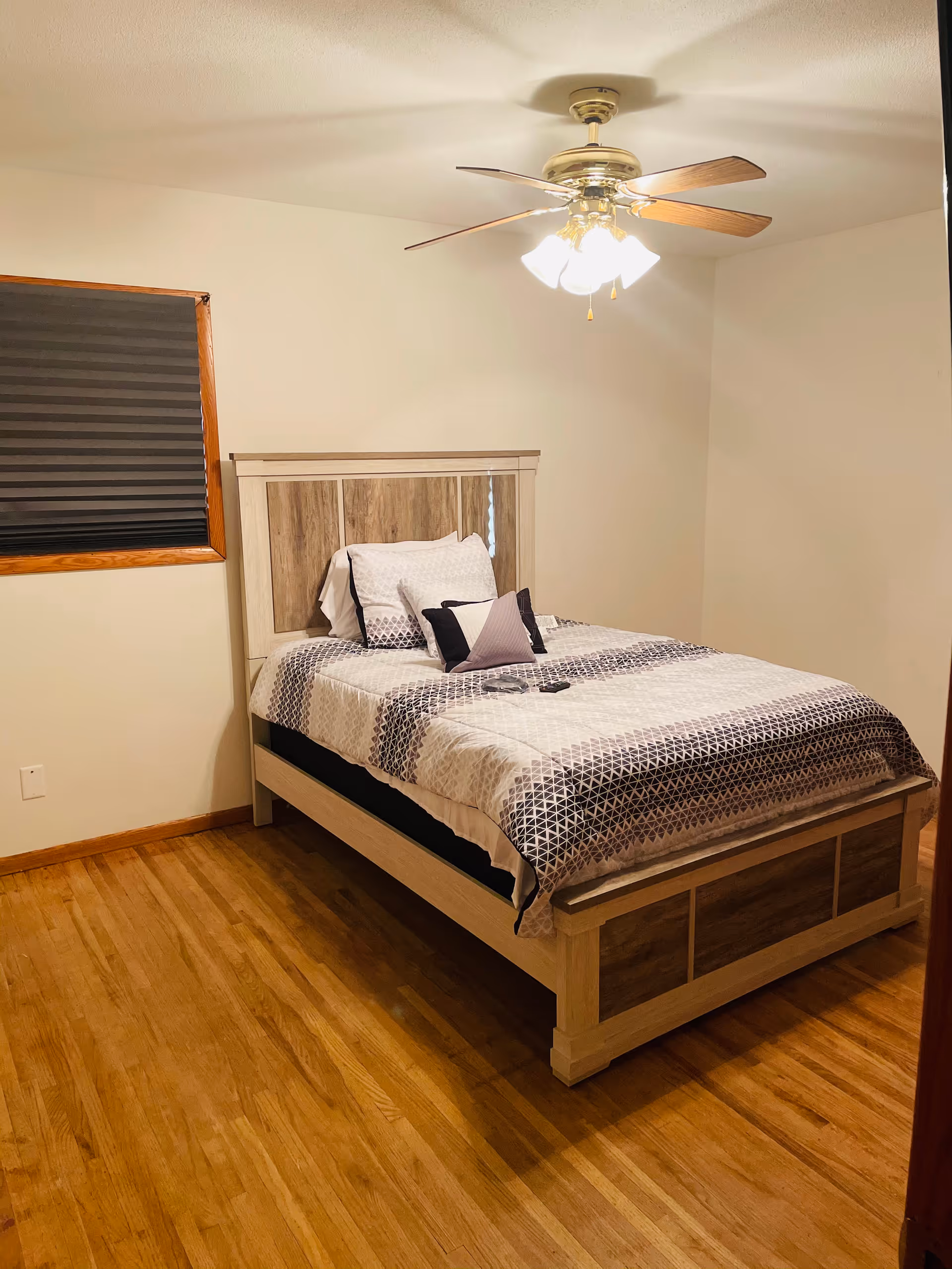 A furnished bedroom with a wooden bed, ceiling fan, and hardwood floors.