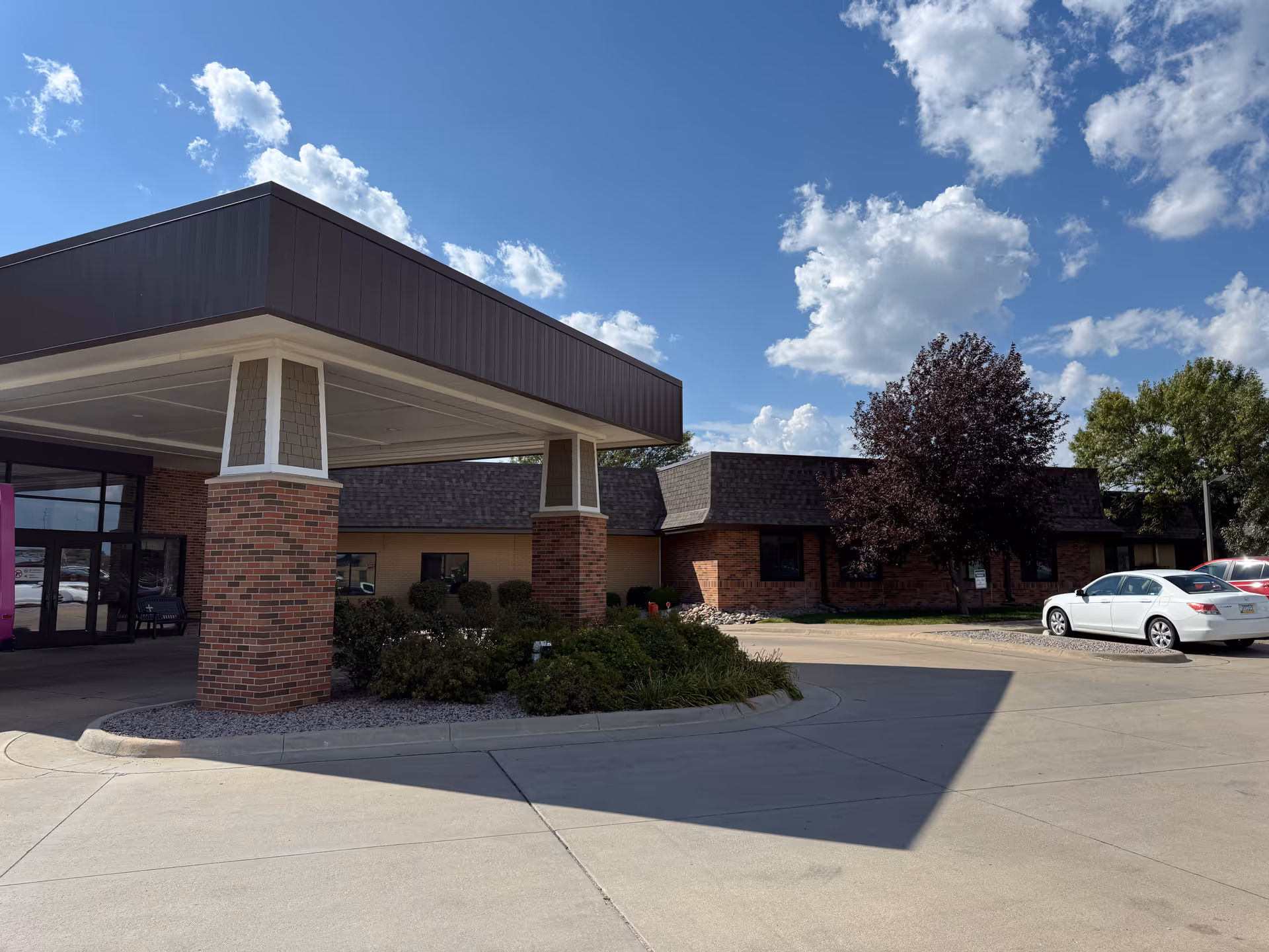 Exterior view of Ascension Living Via Christi Village entrance with brick columns and parked cars.