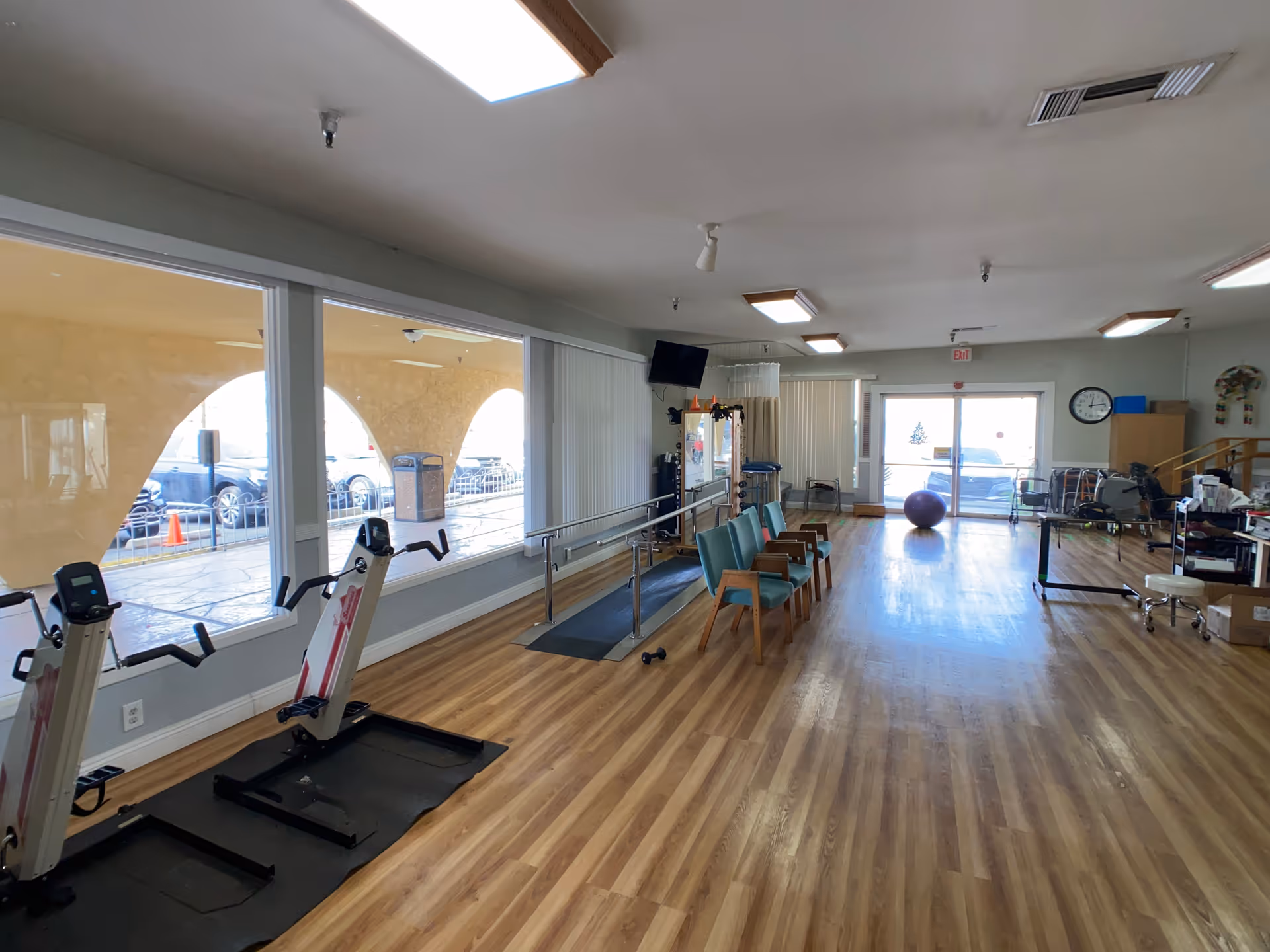 Senior living facility exercise room with treadmills, chairs, and fitness equipment along wooden floor.