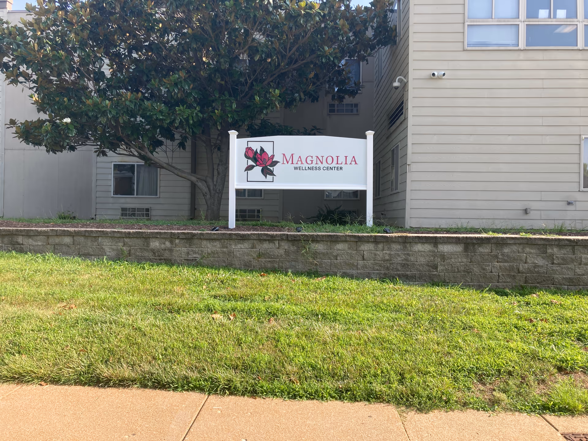 Exterior view of Magnolia Wellness Center sign in front of a beige building with greenery.