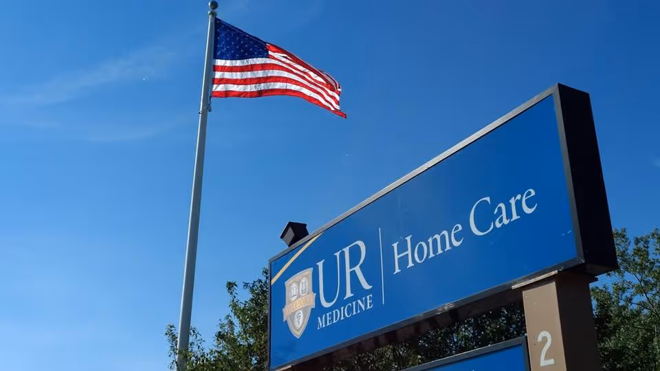 Outdoor view of a UR Medicine Home Care sign with an American flag on a pole.