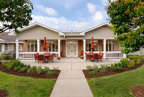 Front view of Cobblestone Manor Assisted Living, a single-story building with outdoor seating tables and umbrellas.