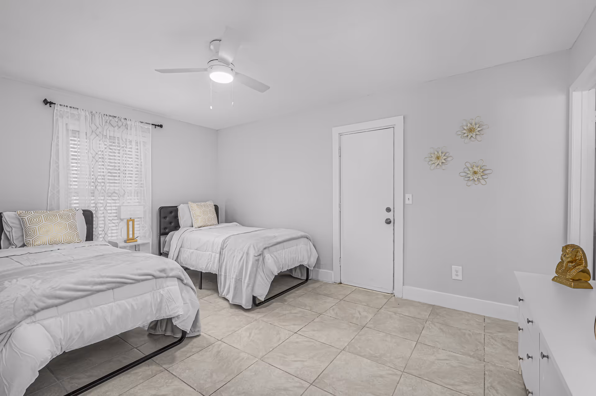 Two twin beds in a bright, minimalist bedroom with tile floor and ceiling fan.