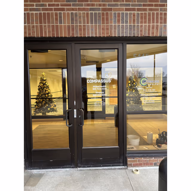 Glass entrance doors of Compassus Home Health with Christmas trees visible inside.