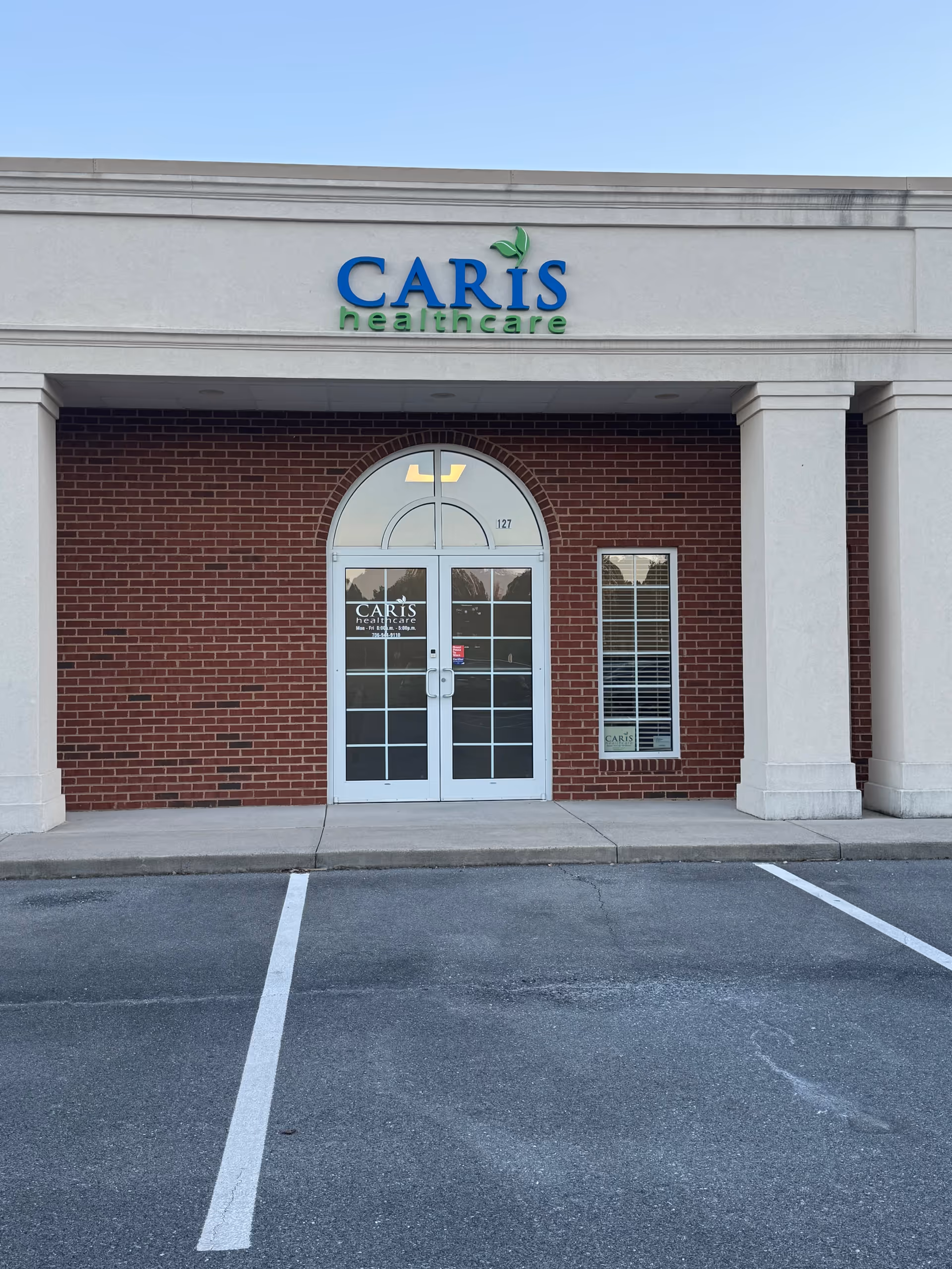 Exterior view of Caris Healthcare facility front with brick wall and arched glass doors.
