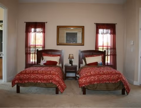 Two single beds with red bedding flank a nightstand lamp beneath a wall mirror.