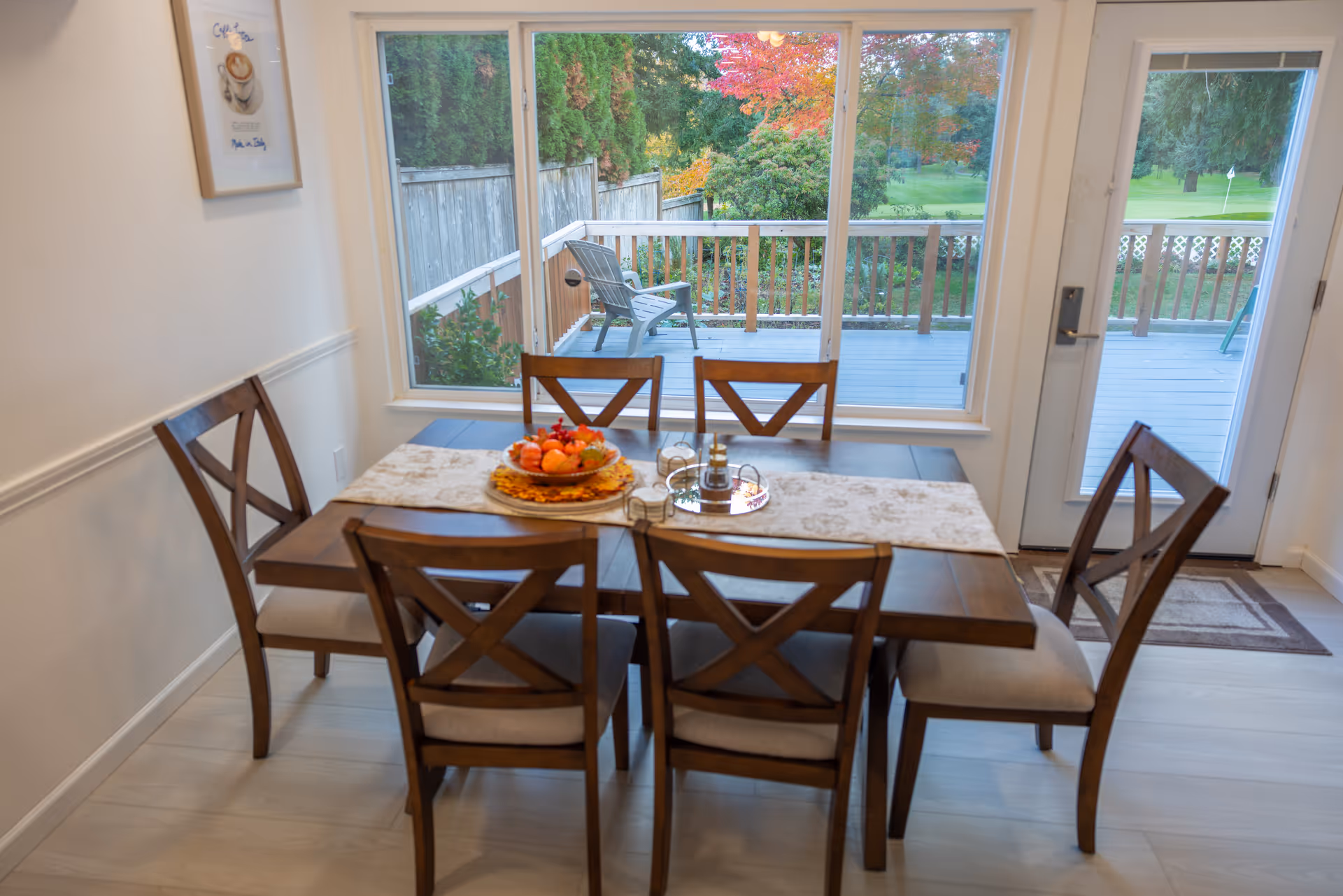Dining room with a wooden table and six chairs, overlooking a deck and greenery outside.