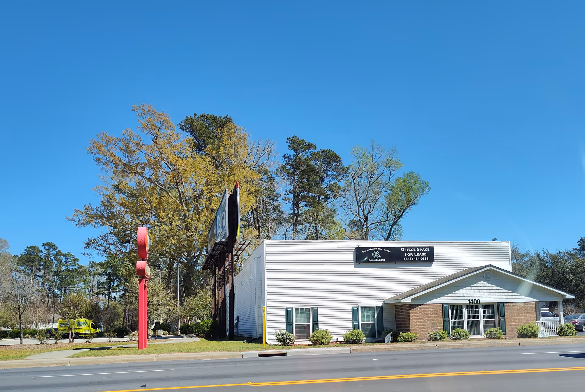 Exterior view of a white building with brick entry, shrubs, and clear blue sky.