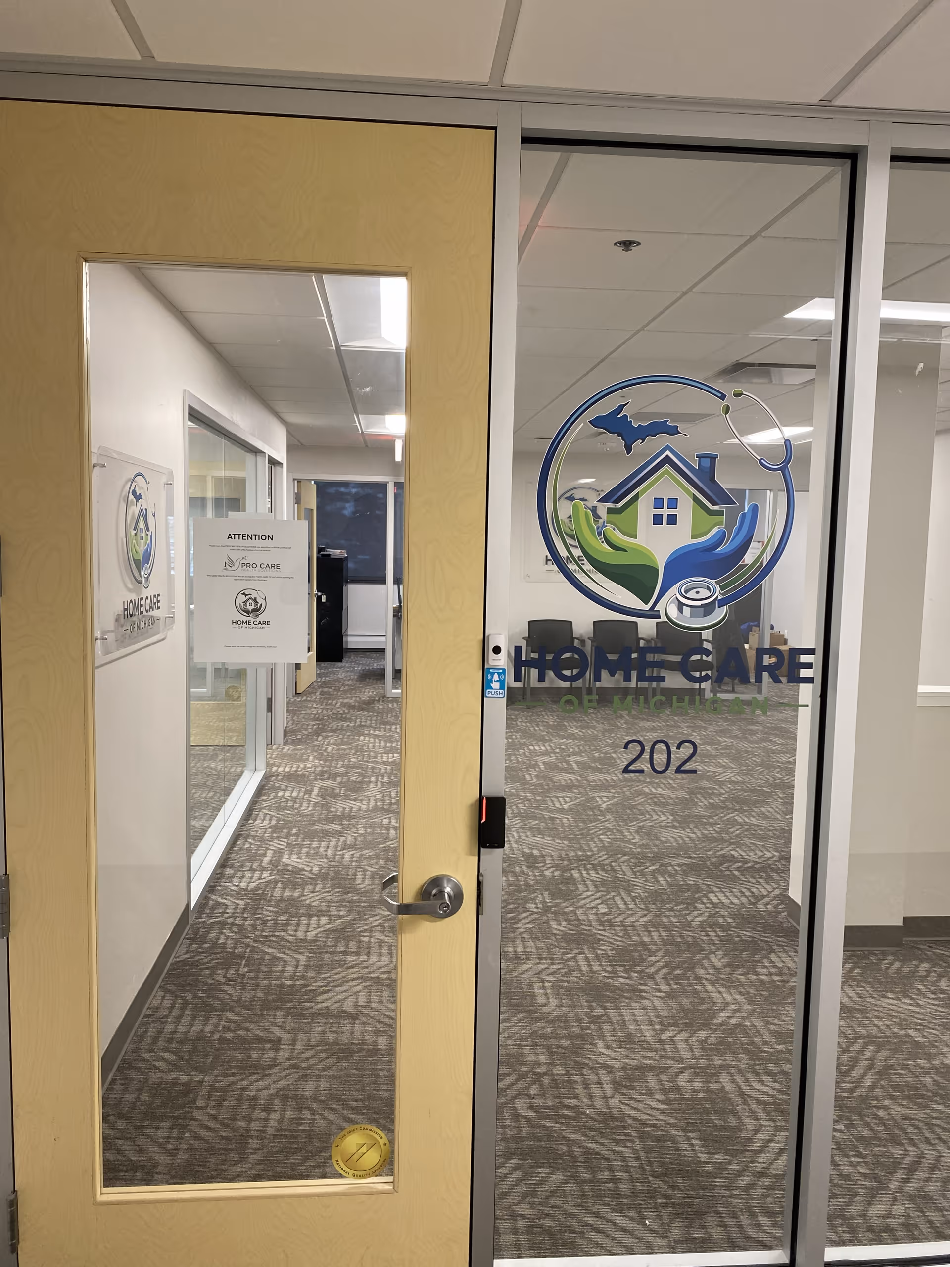 Interior hallway with a glass door bearing Home Care of Michigan logo and room 202.